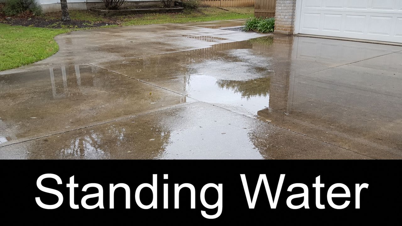 Rainwater collecting in a puddle on a residential concrete driveway in front of a house garage.