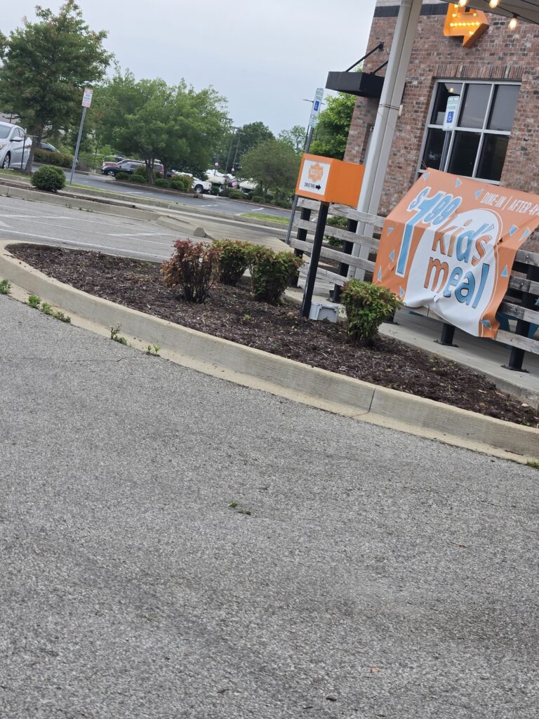 Restaurant exterior with an orange 'Kids meal' banner and nearby parking lot seen at an angle in the foreground.