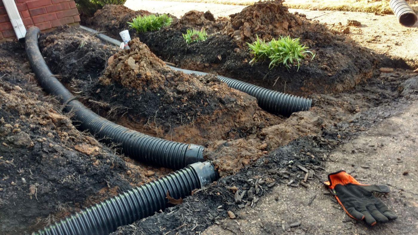 Black corrugated drain pipe laid in freshly dug trenches in a yard during drainage installation