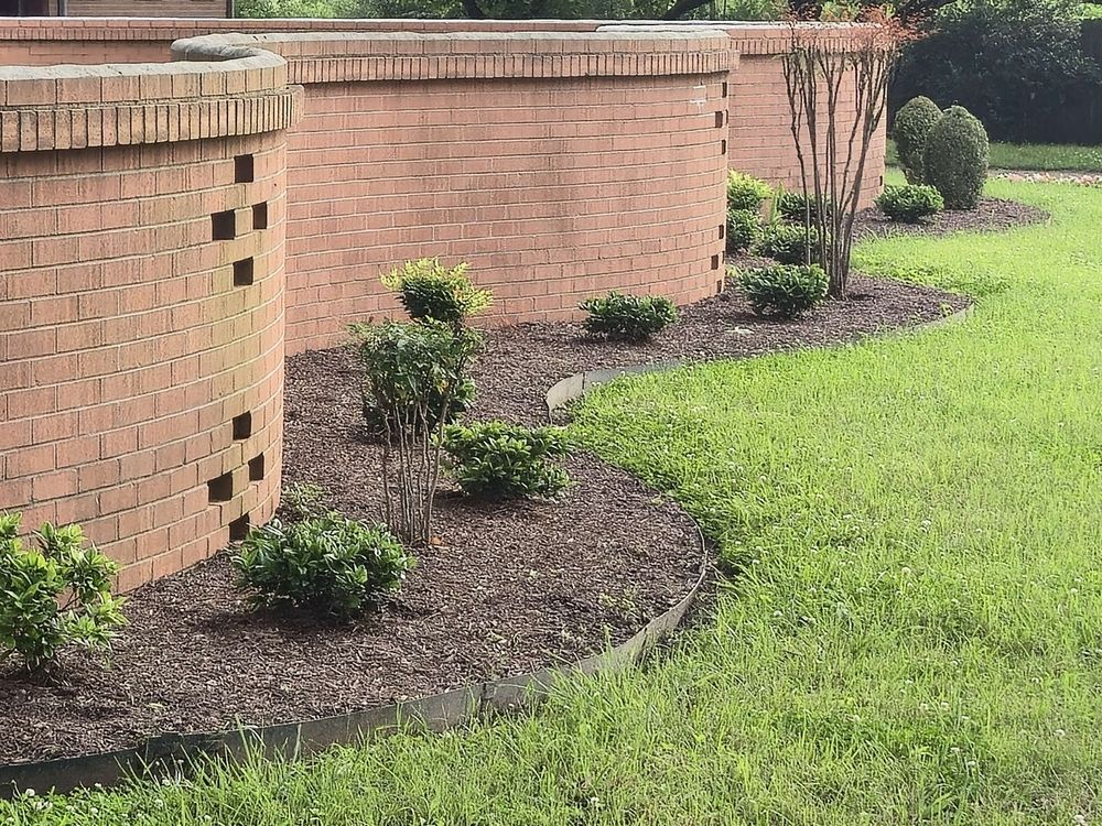 Fresh mulch beds with small shrubs along a curved brick wall, with a neatly edged green lawn