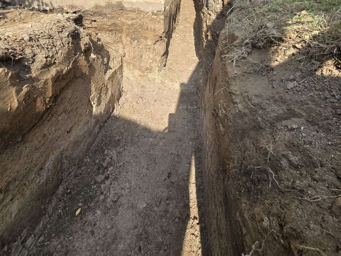 Long, narrow trench dug through soil in a yard